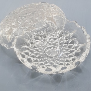 May include: A clear glass dish with a decorative, diamond-shaped pattern. The dish has a raised rim and a scalloped edge.
