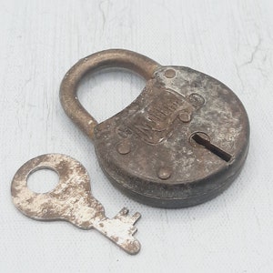 May include: An antique, weathered padlock with a matching key. The lock is a tarnished bronze color with the word "Miller" embossed on the front. The key is a similar color and shows signs of age and use. The lock is closed.