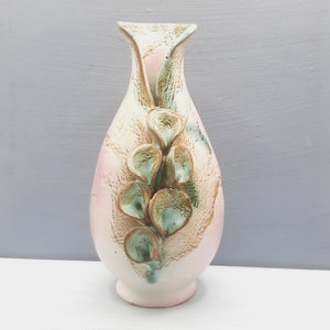 May include: A white ceramic vase with a unique design featuring raised green and gold floral accents. The vase has a narrow neck and a wide, rounded base.