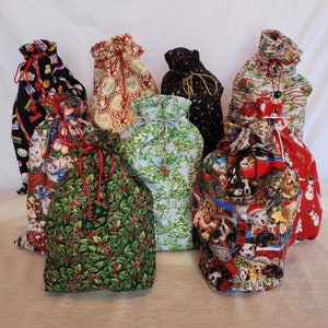 May include: Eight colorful fabric gift bags with drawstring closures. The bags feature various holiday-themed patterns, including holly, snowflakes, and animals.