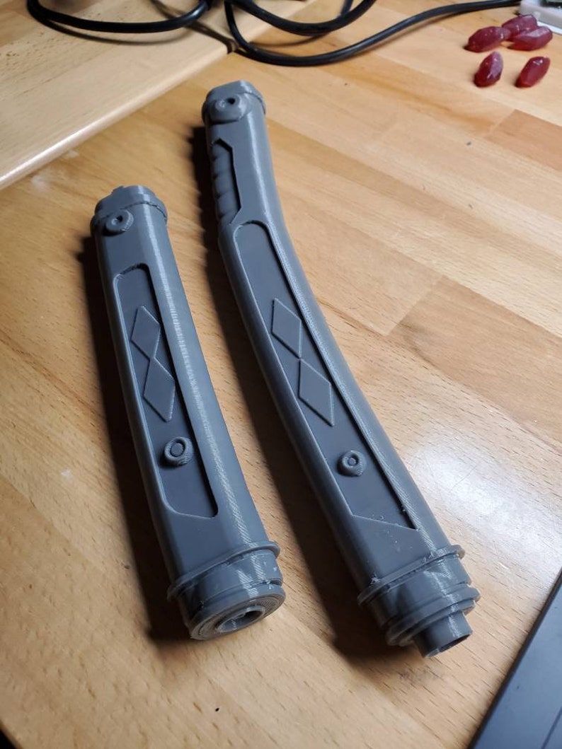 May include: Two gray plastic lightsaber hilts with diamond-shaped patterns. The hilts are curved and have a textured surface.