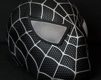 May include: Black and silver Spider-Man mask with a web design. The mask has a mesh eye covering.