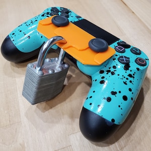 May include: A turquoise and black video game controller with a padlock attached to a 3D printed orange accessory. The controller has a splatter paint design.