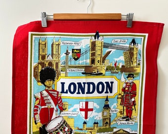 May include: A red tea towel featuring a colourful illustration of London landmarks, including Big Ben, Tower Bridge, and Westminster Abbey. The text "LONDON" is printed in blue letters.