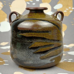 Peut inclure: Un vase en céramique brun et noir avec deux anses. Le vase a un glaçage marbré avec des stries brunes, noires et blanches.
