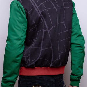 May include: A black bomber jacket with a map print on the back. The jacket has green sleeves and a red collar and waistband. The back of the jacket has the text "54 KINGDOMS 2022" in gold lettering.