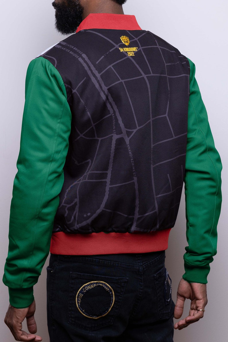 May include: A black bomber jacket with a map print on the back. The jacket has green sleeves and a red collar and waistband. The back of the jacket has the text "54 KINGDOMS 2022" in gold lettering.