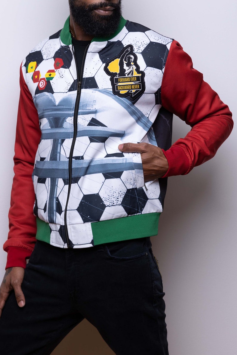 May include: A white, red, and green bomber jacket with a soccer ball pattern. The jacket has a zipper closure and a patch on the left side that says "Forward Ever Backward Never".
