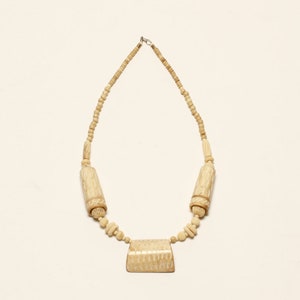 May include: A white ivory necklace with a carved pendant and cylindrical beads.