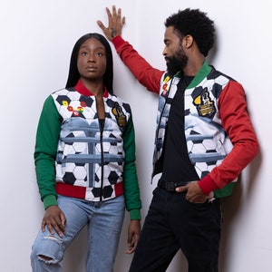 May include: Two people wearing red, green, and white patterned jackets with a soccer ball design. The jackets have a zipper closure and a black background with white soccer balls and a gray design. The jackets also have a green and red sleeve design.