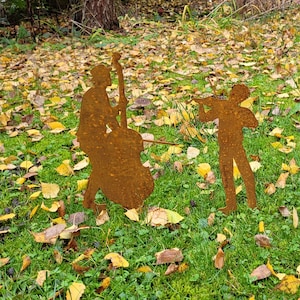 May include: Two rusty metal silhouettes of musicians playing instruments. The musician on the left is playing a cello and the musician on the right is playing a violin. The silhouettes are set against a background of fallen leaves.