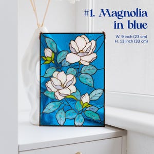 Puede incluir: Panel de vidriera con dise&ntilde;o de magnolia en blanco, azul y verde. La obra de arte rectangular mide 23 cm de ancho y 33 cm de alto. El panel est&aacute; etiquetado como "#1. Magnolia in blue".