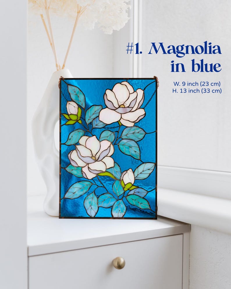Puede incluir: Panel de vidriera con dise&ntilde;o de magnolia en blanco, azul y verde. La obra de arte rectangular mide 23 cm de ancho y 33 cm de alto. El panel est&aacute; etiquetado como "#1. Magnolia in blue".
