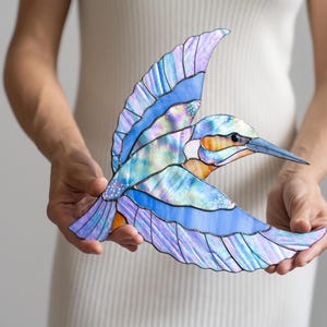 K&ouml;nnte beinhalten: Glasmalerei-Skulptur eines Eisvogels im Flug. Das Kunstwerk hat blaue, violette und schillernde Fl&uuml;gel mit einer orangefarbenen und wei&szlig;en Brust. Der Schnabel ist lang und spitz. Die Skulptur wird vor einem wei&szlig;en Hintergrund gehalten. Die Fl&uuml;gelspannweite betr&auml;gt ca. 25 cm.