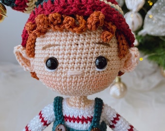 May include: A crocheted elf doll with red and green striped hat, brown hair, and a green and white striped shirt. The doll is wearing blue overalls with brown buttons.