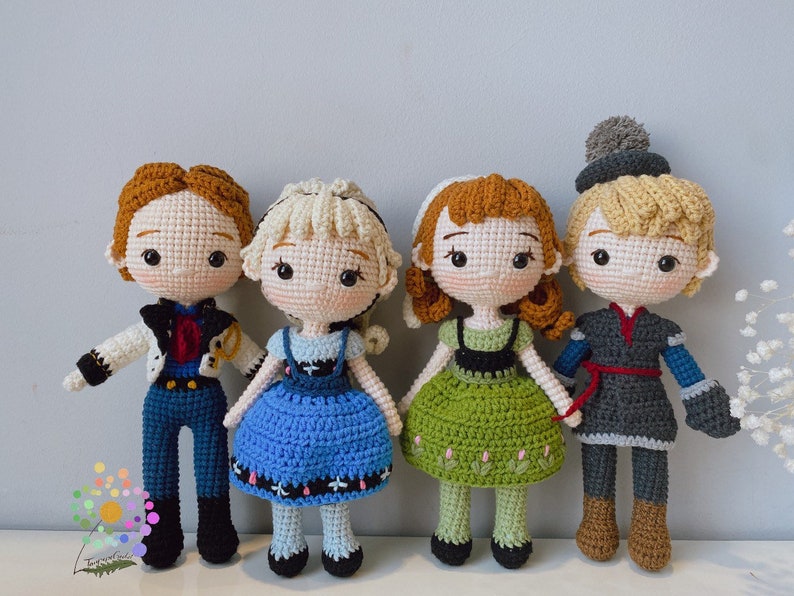 K&ouml;nnte beinhalten: Vier geh&auml;kelte Puppen, die von den Figuren aus dem Film Frozen inspiriert sind. Die Puppen sind in ihren charakteristischen Outfits gekleidet: Elsa in einem blauen Kleid, Anna in einem gr&uuml;nen Kleid, Kristoff in einem braunen und blauen Outfit und Hans in einem grauen und blauen Outfit.