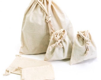 Op de afbeelding: Een verzameling beige canvas zakken met trekkoord in verschillende maten. De zakken hebben een natuurlijke, ongebleekte uitstraling en zijn aan de bovenkant voorzien van een trekkoord. Er zijn verschillende kleinere zakken en een paar platte, open zakjes.
