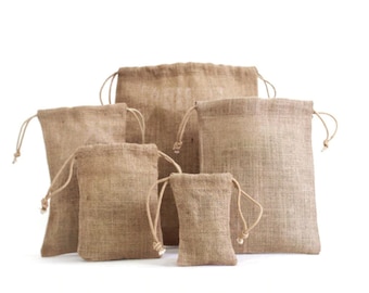 Op de afbeelding: Een verzameling jute trekkoordzakken in verschillende maten. De zakken hebben een natuurlijke bruine kleur met een geweven textuur. Elke zak heeft een bijpassende trekkoordsluiting aan de bovenkant.