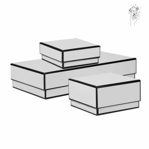 May include: Four white gift boxes with black trim are arranged on a white background. The boxes vary in size, with a rectangular box in the back, a square box on top, and two other boxes in front.