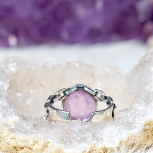 May include: A silver ring featuring a light purple oval gemstone set in a chain link design.