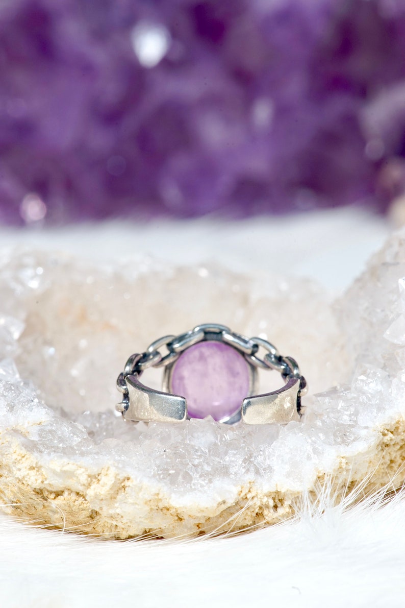 May include: A silver ring featuring a light purple oval gemstone set in a chain link design.