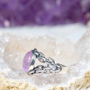 May include: A silver ring featuring a light purple oval gemstone set in a chain link design.