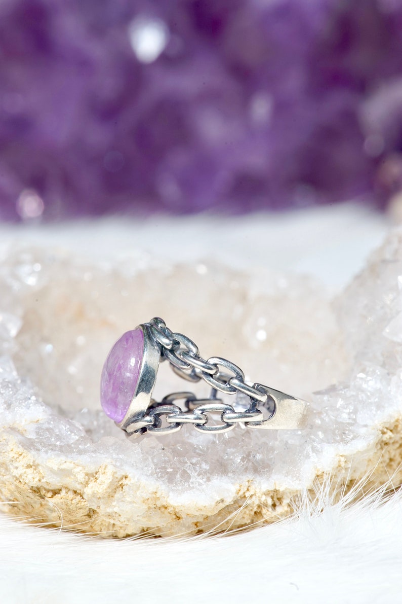 May include: A silver ring featuring a light purple oval gemstone set in a chain link design.