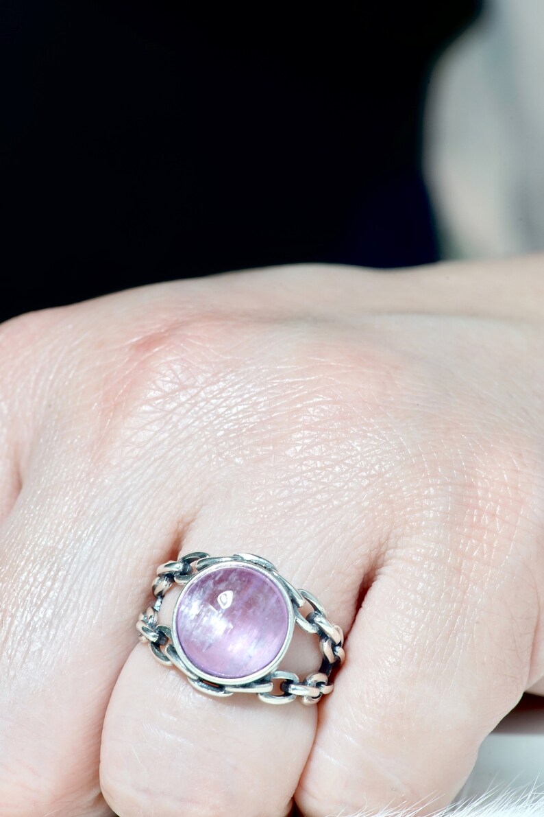 May include: A silver ring featuring a pink gemstone set within a chain-link design.