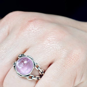 May include: A silver ring with a pink gemstone set in a chain-link design.