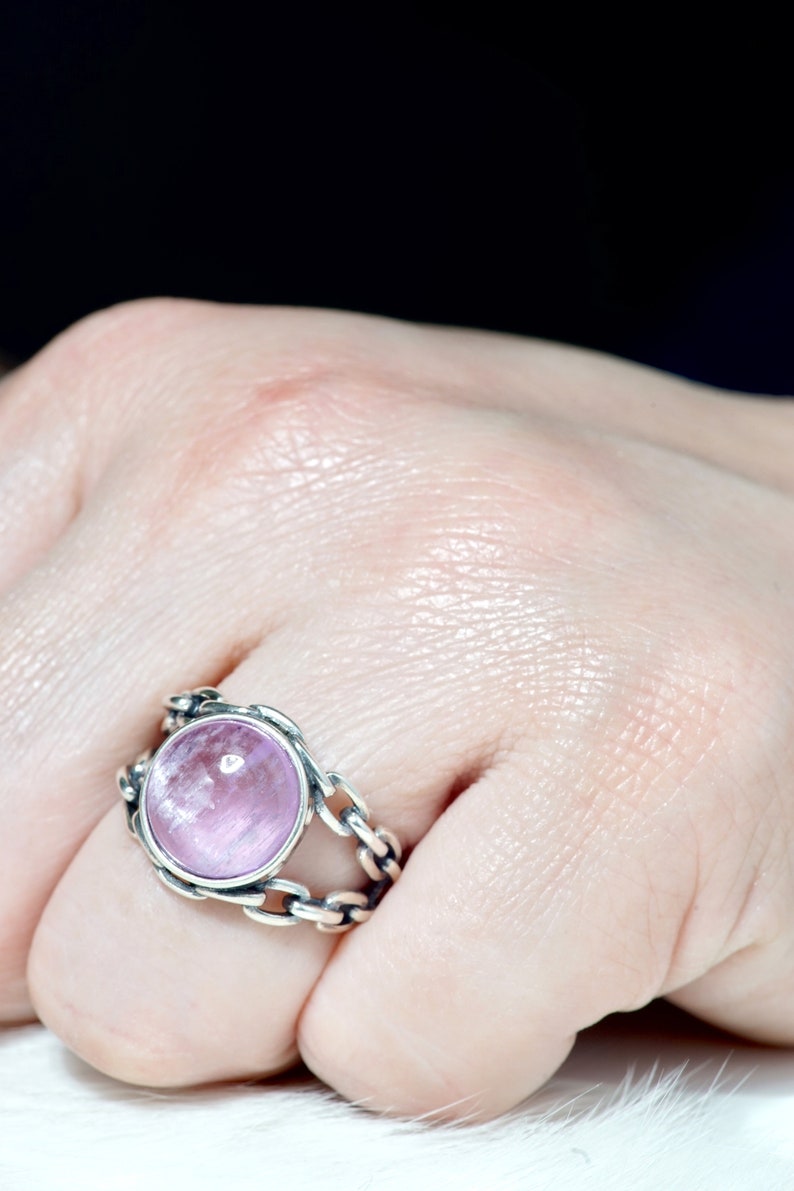 May include: A silver ring with a pink gemstone set in a chain-link design.