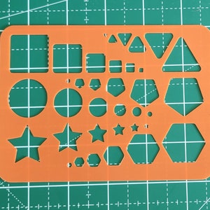 Könnte beinhalten: Orangefarbene Kunststoffschablone mit verschiedenen ausgeschnittenen Formen, darunter Kreise, Sterne, Dreiecke, Sechsecke und Quadrate.