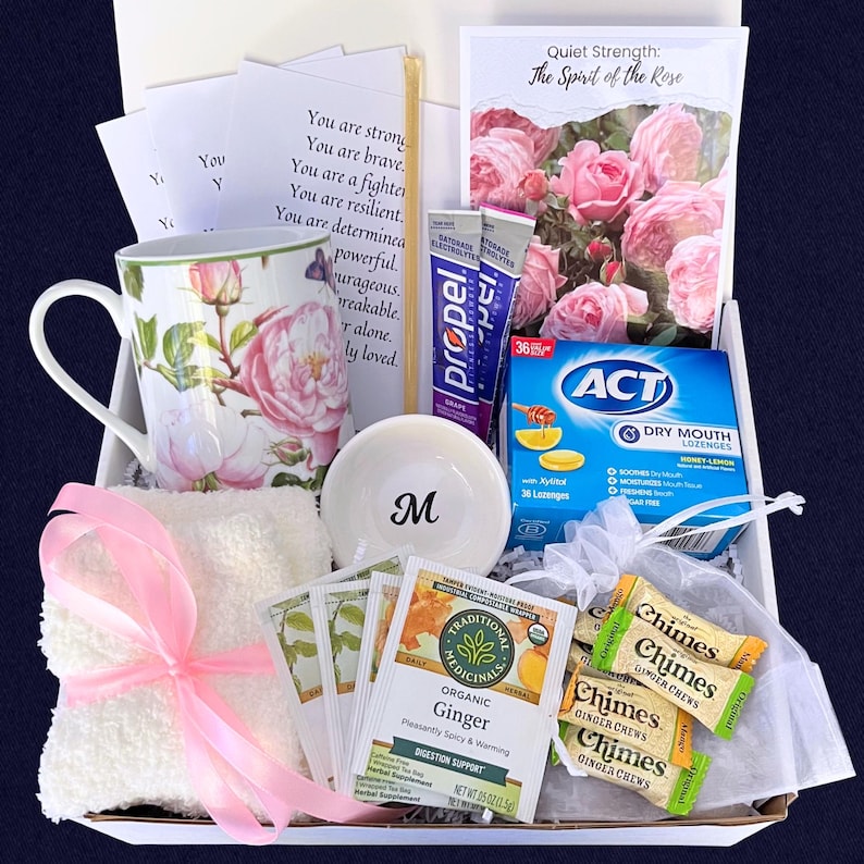 Puede incluir: Una caja de regalo llena de art&iacute;culos de cuidado personal. Incluye una taza floral, un cuenco blanco peque&ntilde;o con una "M", un pa&ntilde;o blanco atado con una cinta rosa, bolsitas de t&eacute;, caramelos de jengibre y una tarjeta con el texto "Quiet Strength: The Spirit of the Rose".