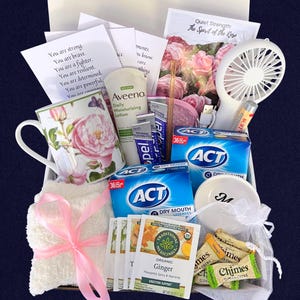 Puede incluir: Una cesta de regalo con art&iacute;culos de cuidado personal. Incluye una taza floral, loci&oacute;n Aveeno, pastillas para la boca seca ACT, t&eacute; de jengibre, un ventilador peque&ntilde;o, b&aacute;lsamo labial y tarjetas inspiradoras. La cesta est&aacute; atada con una cinta rosa.