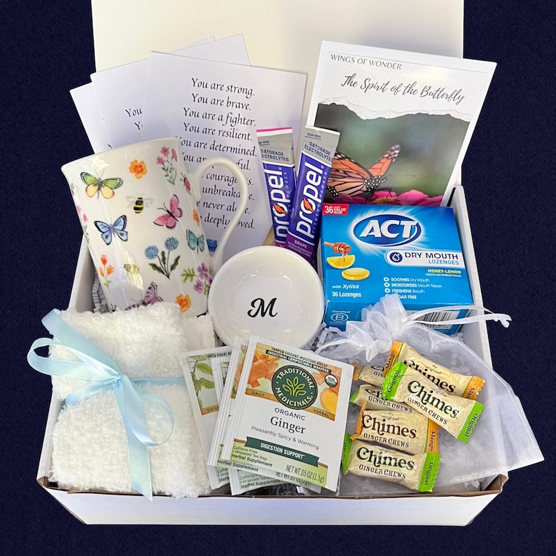 Puede incluir: Una caja de regalo llena de una taza floral, un cuenco blanco peque&ntilde;o con la letra "M", un pa&ntilde;o blanco atado con una cinta azul, sobres de t&eacute;, paquetes de electrolitos Propel, pastillas para la boca seca ACT y caramelos de jengibre. La caja tambi&eacute;n contiene una tarjeta con texto inspirador y un folleto titulado "El Esp&iacute;ritu de la Mariposa."