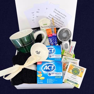 Peut inclure: Un panier cadeau de bien-&ecirc;tre avec une tasse &agrave; carreaux verts, un petit bol blanc avec un "W", une serviette noire avec un ruban cr&egrave;me, des pastilles ACT pour la bouche s&egrave;che, de la lotion Aveeno et d'autres produits.