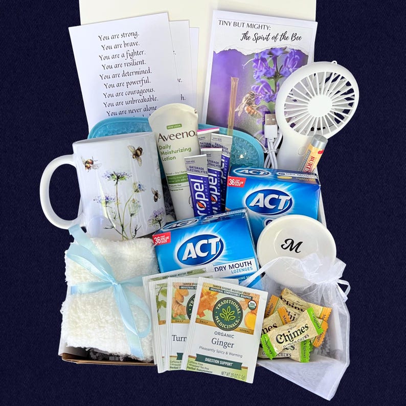 Puede incluir: Una cesta de regalo llena de art&iacute;culos de cuidado personal. Incluye una taza con abejas y flores, loci&oacute;n Aveeno, pastillas para la boca seca ACT, t&eacute; de jengibre, un ventilador peque&ntilde;o y un platillo peque&ntilde;o con la letra "M".
