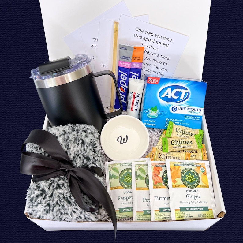 Peut inclure: Coffret cadeau de soins personnels. Il comprend un mug noir, un petit bol blanc avec un "w", des sachets de th&eacute;, des pastilles et une &eacute;charpe grise duveteuse nou&eacute;e avec un ruban noir. Contient aussi un tube d'Aquaphor et des sachets Propel.