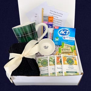 Peut inclure: Un coffret cadeau contenant une tasse &agrave; carreaux verts, un petit bol blanc avec un "W", des chaussettes noires nou&eacute;es avec un ruban cr&egrave;me, des sachets de th&eacute;, des pastilles et des bonbons au gingembre. La bo&icirc;te contient une note avec du texte.