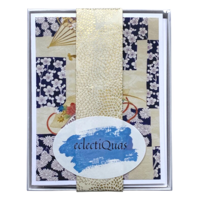 Pode incluir: Um conjunto de cart&otilde;es com um design de inspira&ccedil;&atilde;o japonesa. Os cart&otilde;es apresentam um padr&atilde;o de patchwork com motivos florais e de leques em creme, azul marinho e dourado. O conjunto &eacute; embrulhado com uma faixa dourada e tem o texto "electiQuas" num oval azul.