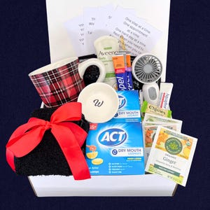 Peut inclure: Un coffret cadeau rempli d'articles de soins personnels. Comprend une tasse &agrave; carreaux, un petit bol blanc avec un "W", une serviette noire avec un n&oelig;ud rouge, une cr&egrave;me hydratante Aveeno, des pastilles ACT pour la s&eacute;cheresse buccale, un petit ventilateur et du th&eacute;.