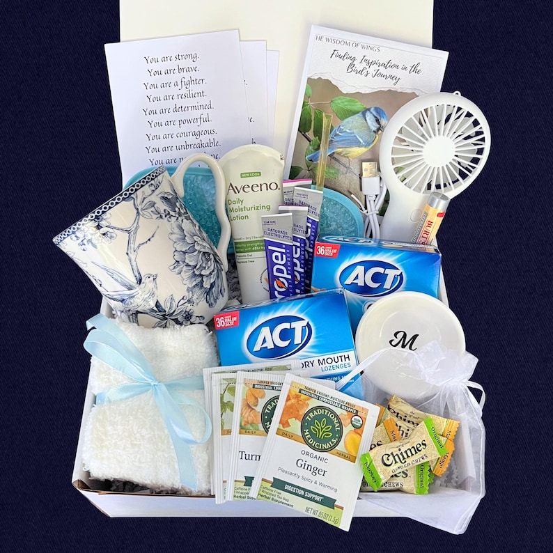 Puede incluir: Una cesta de regalo llena de art&iacute;culos de cuidado personal. Incluye una taza de t&eacute; floral, loci&oacute;n Aveeno, pastillas ACT, un peque&ntilde;o ventilador, bolsitas de t&eacute; y un plato blanco peque&ntilde;o con la letra "M". Tambi&eacute;n se incluye una tarjeta con texto inspirador.