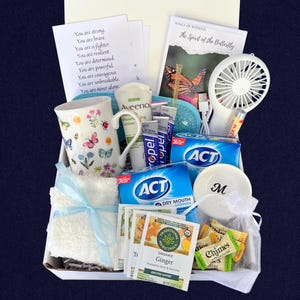 Puede incluir: Una cesta de regalo llena de art&iacute;culos de cuidado personal. Incluye una taza floral, loci&oacute;n Aveeno, pastillas para la boca seca ACT, t&eacute; de jengibre, un ventilador peque&ntilde;o, b&aacute;lsamo labial y una tarjeta con texto inspirador. Tambi&eacute;n se incluye una tapa blanca con la letra "M".