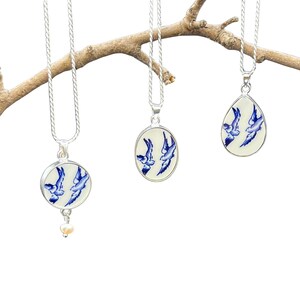 May include: Three silver necklaces with blue and white porcelain pendants featuring a design of three birds in flight. The pendants are round, oval, and teardrop shaped.