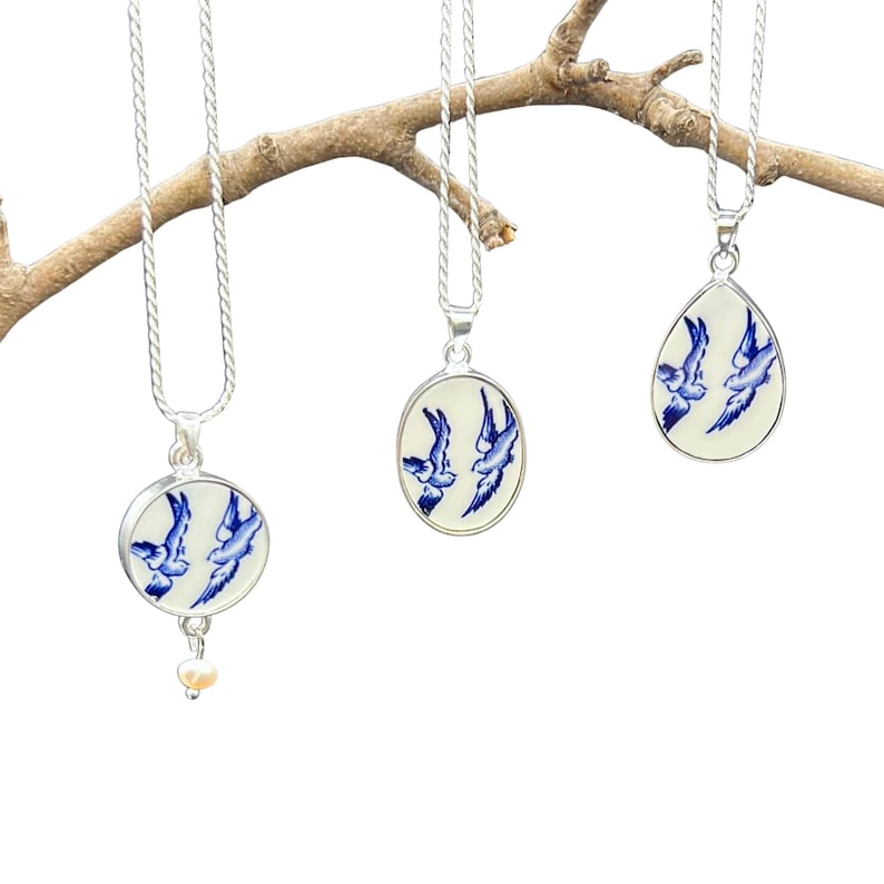 May include: Three silver necklaces with blue and white porcelain pendants featuring a design of three birds in flight. The pendants are round, oval, and teardrop shaped.