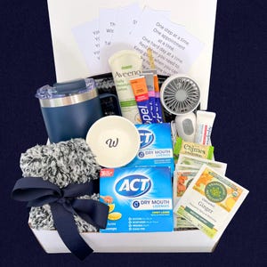 Peut inclure: Un coffret cadeau rempli d'articles de soins personnels. Comprend un gobelet bleu marine, un petit bol blanc avec un "W", une &eacute;charpe floue grise et blanche avec un n&oelig;ud bleu marine, de la lotion, des pastilles, du th&eacute; et un petit ventilateur. Le coffret contient des notes inspirantes.