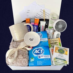 Peut inclure: Un coffret cadeau contenant une tasse blanche, un petit bol avec un "w", une couverture douce avec un ruban cr&egrave;me, des pastilles pour la bouche s&egrave;che ACT, de la lotion Aveen, des bonbons au gingembre et un petit ventilateur.