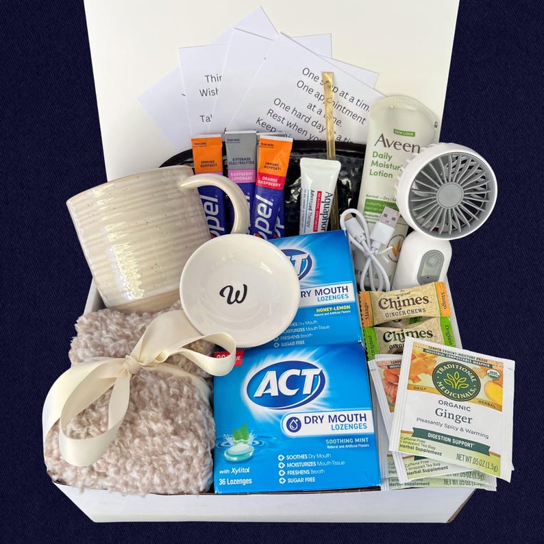 Peut inclure: Un coffret cadeau contenant une tasse blanche, un petit bol avec un "w", une couverture douce avec un ruban cr&egrave;me, des pastilles pour la bouche s&egrave;che ACT, de la lotion Aveen, des bonbons au gingembre et un petit ventilateur.