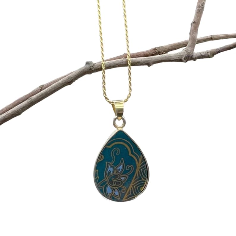 K&ouml;nnte beinhalten: Eine goldene Kettenkette mit einem tropfenf&ouml;rmigen Anh&auml;nger. Der Anh&auml;nger ist aus gr&uuml;nem Stein mit einem goldenen Blumendesign.