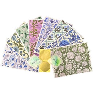 May include: A collection of rectangular greeting cards featuring various floral and botanical patterns in shades of green, pink, blue, and white. Included are two circular stickers with the text thank you and two gold circular birthday stickers.