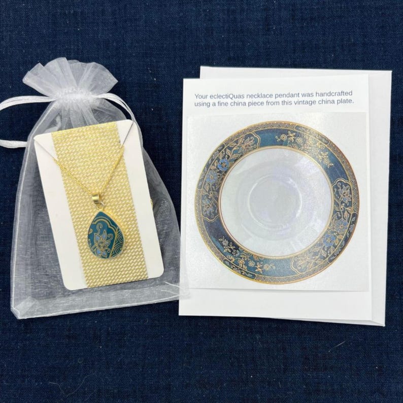 K&ouml;nnte beinhalten: Eine goldene Halskette mit einem t&uuml;rkisfarbenen Anh&auml;nger mit floralem Design. Die Halskette ist in einem wei&szlig;en Organzas&auml;ckchen verpackt und wird mit einer Karte geliefert, auf der steht: "Ihr eclectiQuas-Halskettenanh&auml;nger wurde handgefertigt aus einem St&uuml;ck feinem Porzellan von diesem antiken Porzellanteller."